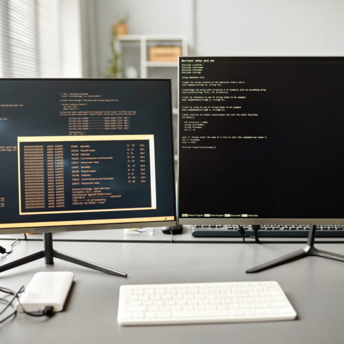 Background image of two computers on desk with code lines on screen in IT developers office, copy space