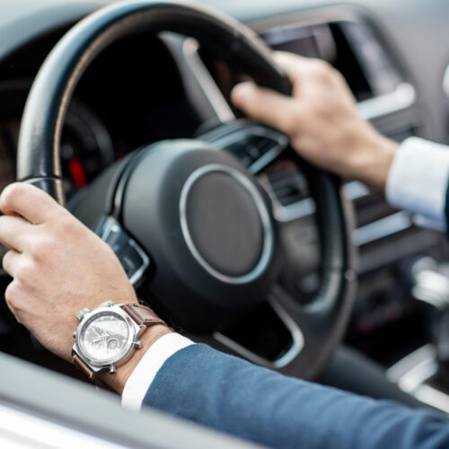 Close-up of businessman's hands on the helm of a luxury car