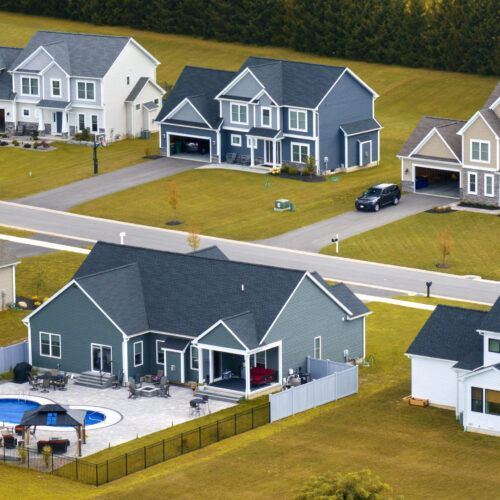 Upscale suburban homes with large backyards and green grassy lawns in summer season. Private residential houses in rural suburban sprawl area in Rochester, New York.